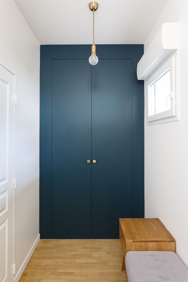 Cette photo montre un petit couloir moderne avec un mur bleu, parquet clair et un sol beige.