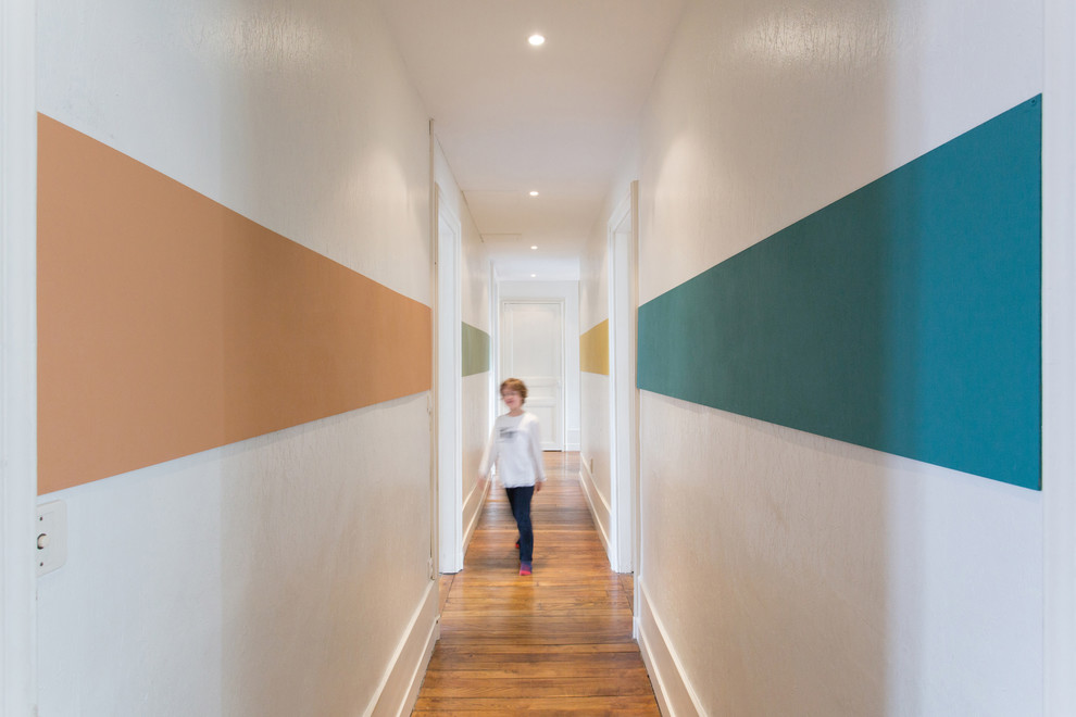 Idée de décoration pour un grand couloir design avec un mur multicolore et un sol en bois brun.