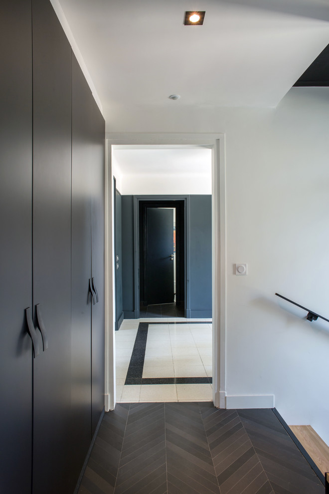 Cette image montre un couloir minimaliste avec un mur blanc, parquet foncé et un sol marron.