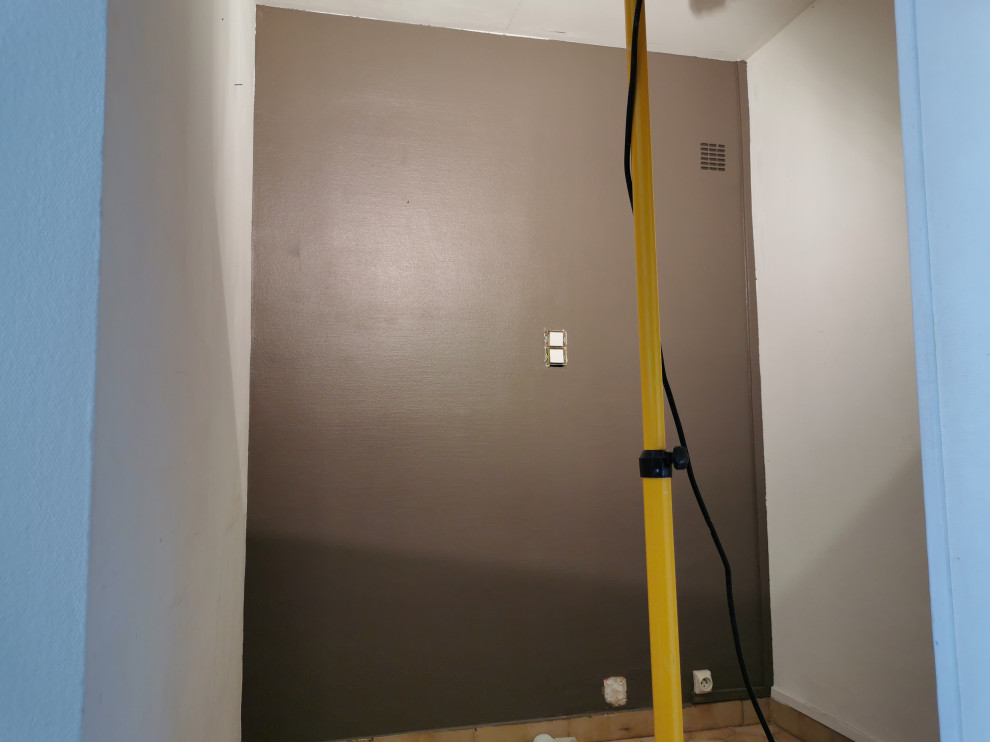 Cette image montre un petit couloir minimaliste avec un mur bleu, tomettes au sol et un sol beige.