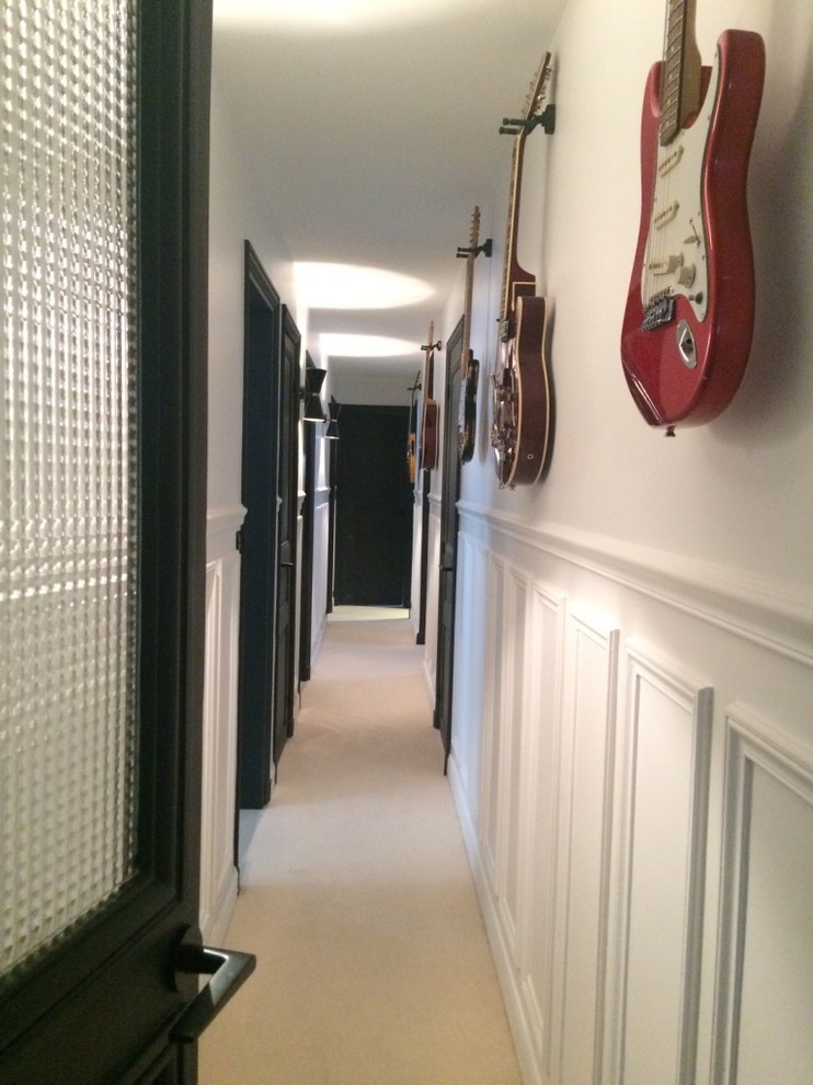 Cette photo montre un grand couloir tendance avec un mur blanc, moquette et un sol beige.