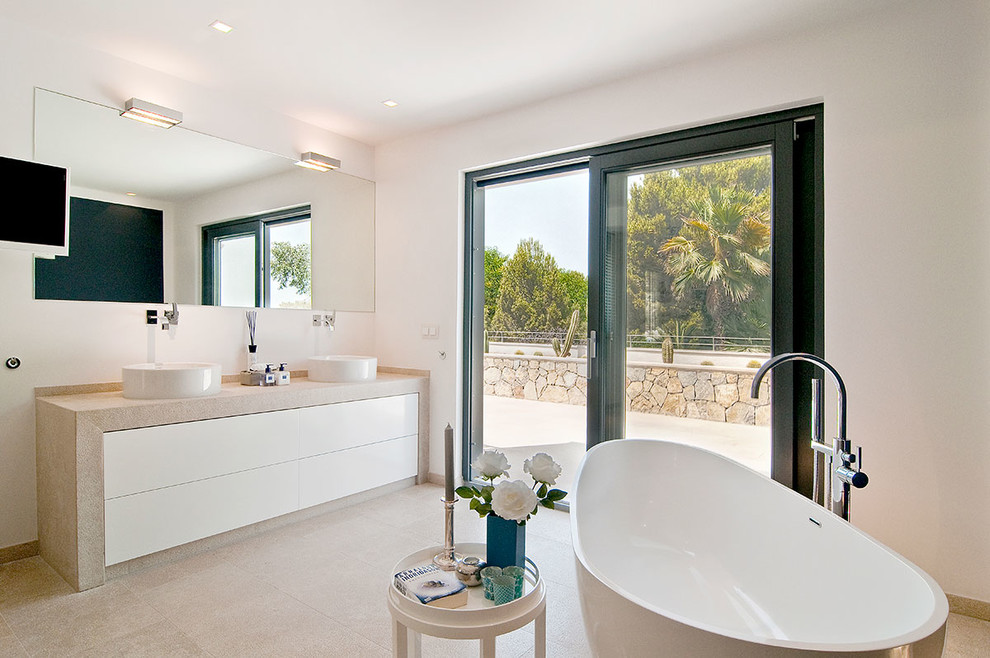 Идея дизайна: ванная комната среднего размера в средиземноморском стиле с плоскими фасадами, белыми фасадами, отдельно стоящей ванной, белыми стенами, полом из известняка, душевой кабиной, настольной раковиной, столешницей из известняка и душем над ванной