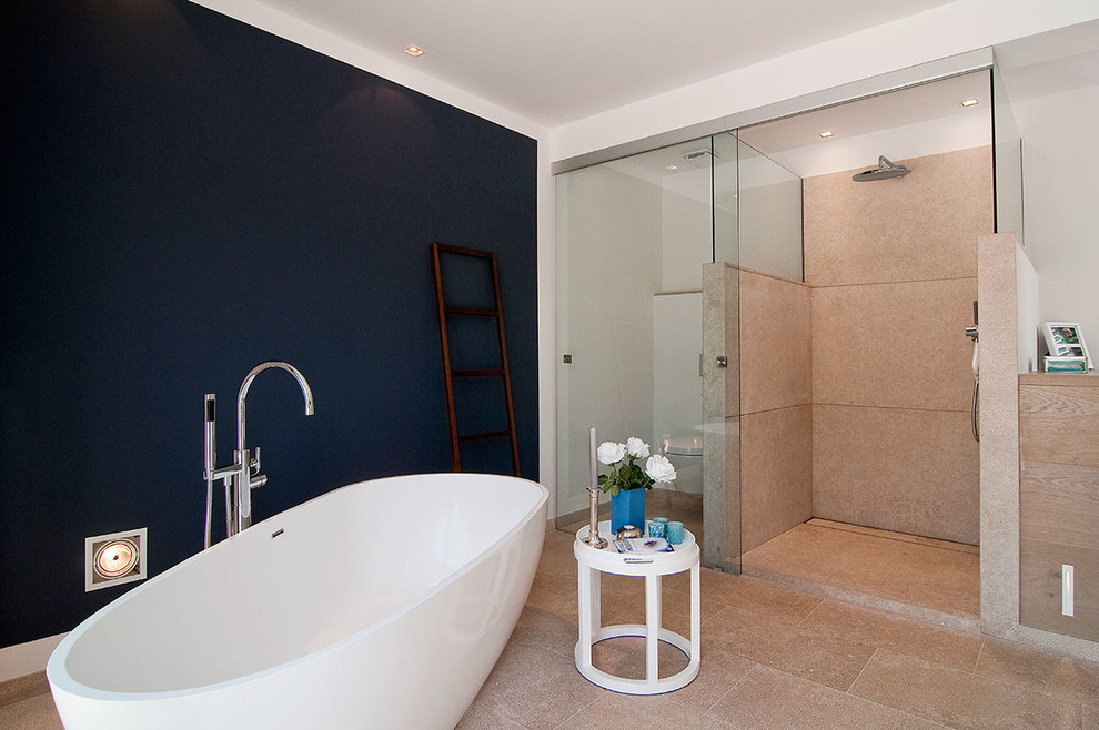 На фото: главная ванная комната среднего размера в современном стиле с светлыми деревянными фасадами, отдельно стоящей ванной, душем без бортиков, бежевой плиткой, синими стенами, инсталляцией, плиткой из листового камня и полом из известняка