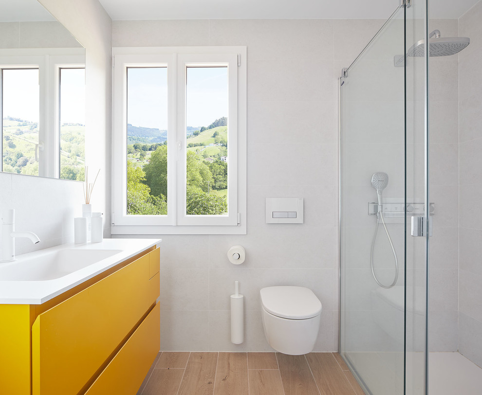 This is an example of a medium sized modern ensuite bathroom in Other with freestanding cabinets, yellow cabinets, a built-in shower, a wall mounted toilet, brown tiles, ceramic tiles, white walls, porcelain flooring, an integrated sink, engineered stone worktops, beige floors, a sliding door and white worktops.