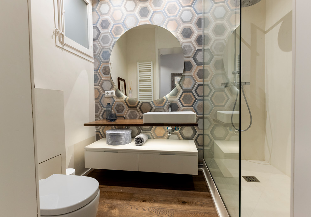 Modernes Badezimmer mit flächenbündigen Schrankfronten, weißen Schränken, farbigen Fliesen, weißer Wandfarbe, braunem Holzboden, Aufsatzwaschbecken, Waschtisch aus Holz, braunem Boden, Falttür-Duschabtrennung und brauner Waschtischplatte in Barcelona