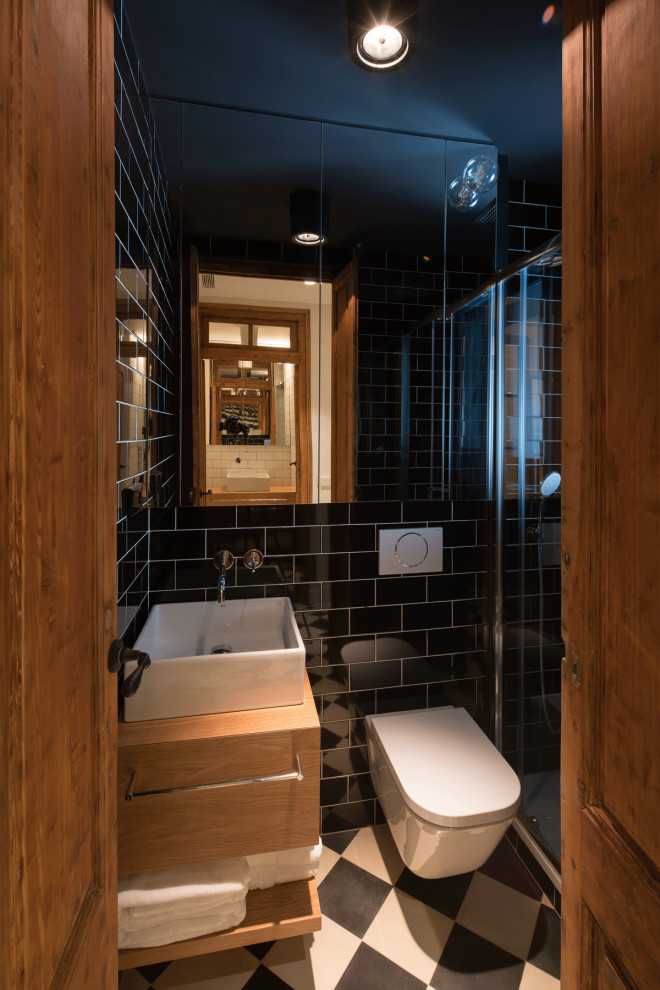 Idéer för att renovera ett litet vintage brun brunt badrum med dusch, med luckor med infälld panel, bruna skåp, våtrum, en vägghängd toalettstol, svart kakel, keramikplattor, vita väggar, klinkergolv i keramik, ett fristående handfat, träbänkskiva, vitt golv och dusch med gångjärnsdörr