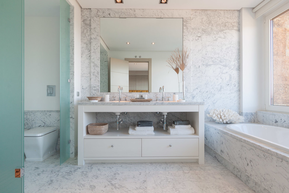 На фото: большая главная ванная комната в морском стиле с плоскими фасадами, белыми фасадами, ванной в нише и монолитной раковиной с