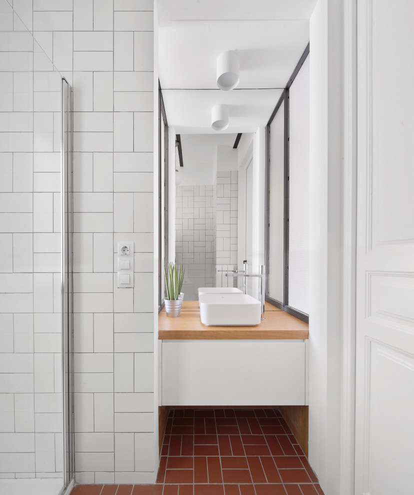 Bild på ett funkis brun brunt badrum, med släta luckor, vita skåp, vit kakel, vita väggar, ett fristående handfat, träbänkskiva och rött golv