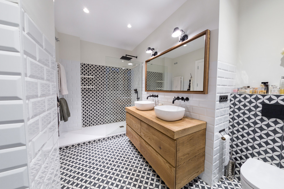 Idéer för att renovera ett mellanstort funkis brun brunt badrum med dusch, med släta luckor, keramikplattor, vita väggar, träbänkskiva, vit kakel, svart och vit kakel, med dusch som är öppen, skåp i ljust trä, en dusch i en alkov, en vägghängd toalettstol, ett fristående handfat och flerfärgat golv