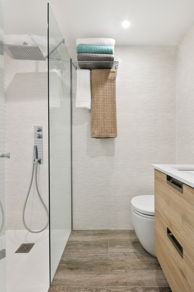 Immagine di una stanza da bagno con doccia moderna con ante in legno chiaro, doccia a filo pavimento, orinatoio, piastrelle bianche, piastrelle in gres porcellanato, pareti bianche, pavimento in gres porcellanato e lavabo sottopiano