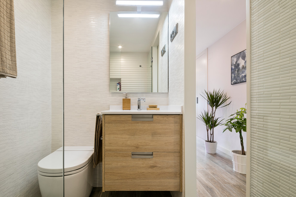 Источник вдохновения для домашнего уюта: маленькая ванная комната в стиле модернизм с светлыми деревянными фасадами, душем без бортиков, писсуаром, белой плиткой, керамогранитной плиткой, белыми стенами, полом из керамогранита, душевой кабиной, врезной раковиной, столешницей из искусственного кварца и душем с распашными дверями для на участке и в саду
