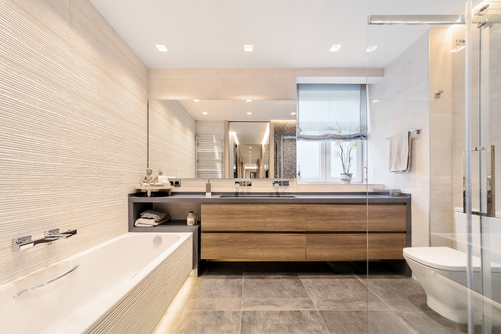 Mittelgroßes Modernes Badezimmer En Suite mit dunklen Holzschränken, grauem Boden, grauer Waschtischplatte, flächenbündigen Schrankfronten, Einbaubadewanne, Toilette mit Aufsatzspülkasten, beigen Fliesen und beiger Wandfarbe in Bilbao