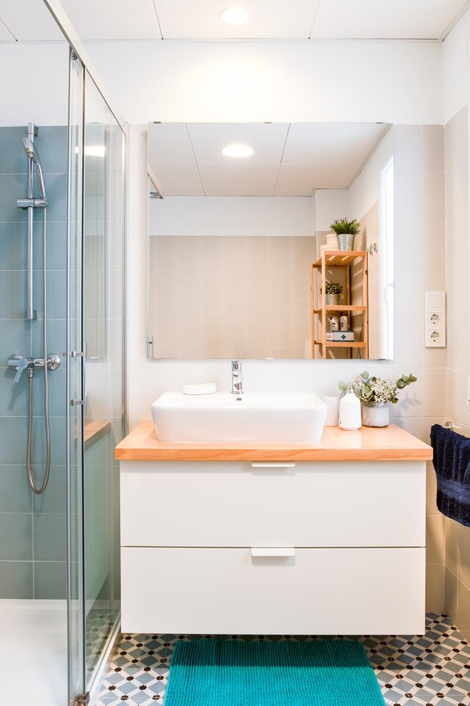 Стильный дизайн: ванная комната в белых тонах с отделкой деревом в скандинавском стиле с плоскими фасадами, белыми фасадами, душем в нише, синей плиткой, белыми стенами, настольной раковиной, столешницей из дерева, синим полом, душем с раздвижными дверями и бежевой столешницей - последний тренд