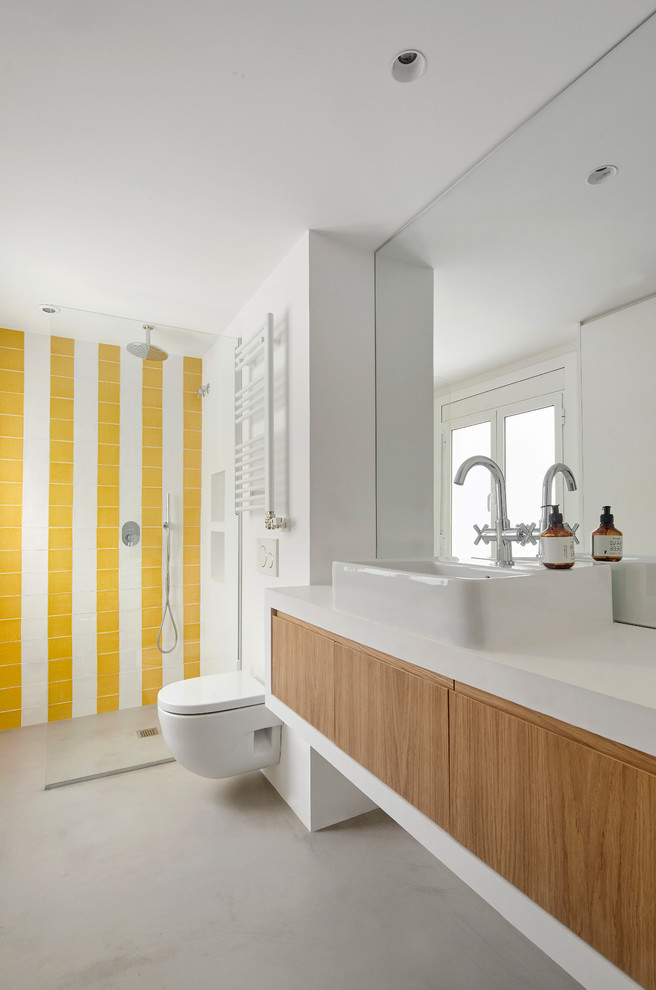 Inredning av ett modernt vit vitt badrum med dusch, med skåp i mellenmörkt trä, en kantlös dusch, en vägghängd toalettstol, gul kakel, vit kakel, vita väggar, betonggolv, ett fristående handfat, grått golv och släta luckor