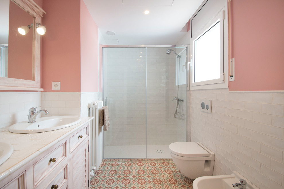Ispirazione per una stanza da bagno con doccia mediterranea con WC a due pezzi, piastrelle bianche, pareti rosa, porta doccia scorrevole, ante a persiana, doccia alcova, pavimento con piastrelle a mosaico, lavabo da incasso e top bianco