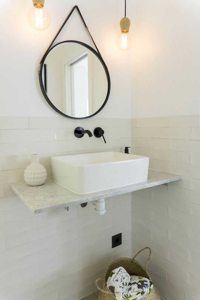 Inredning av ett skandinaviskt litet badrum med dusch, med öppna hyllor, ett badkar i en alkov, en toalettstol med hel cisternkåpa, flerfärgad kakel, keramikplattor, vita väggar, cementgolv, ett fristående handfat, granitbänkskiva och grått golv