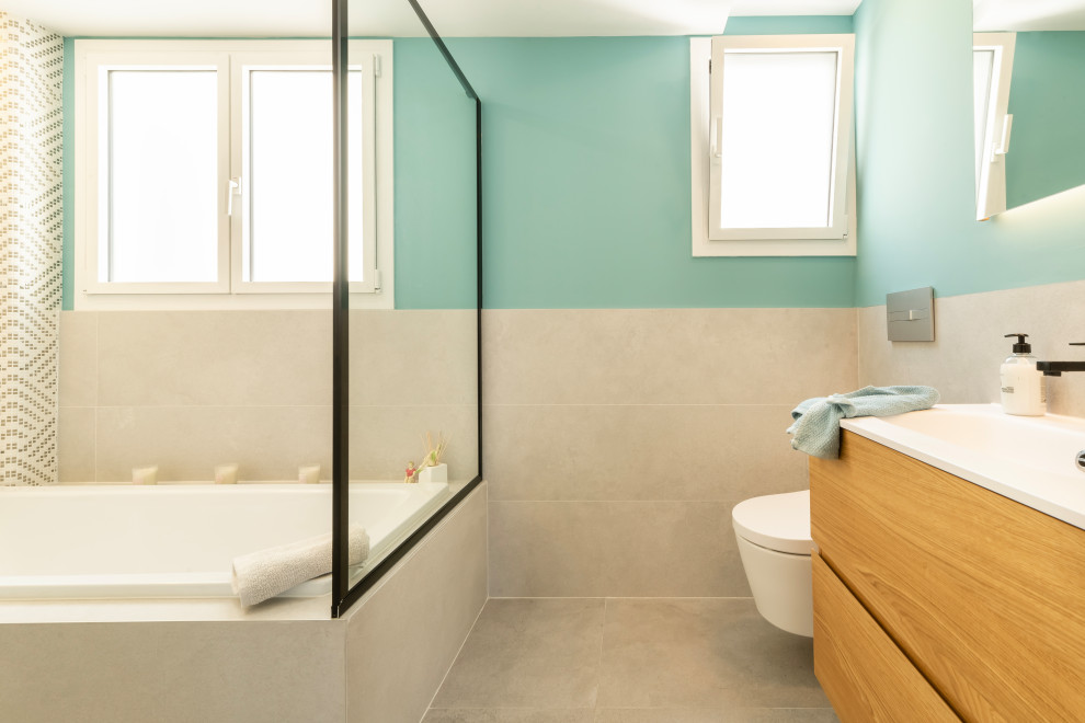 Photo of a medium sized modern family bathroom in Other with flat-panel cabinets, medium wood cabinets, an alcove bath, a walk-in shower, a wall mounted toilet, white tiles, ceramic tiles, green walls, porcelain flooring, an integrated sink, engineered stone worktops, grey floors, a hinged door and white worktops.