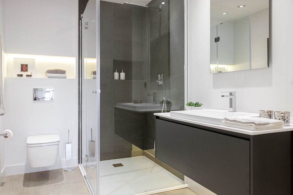 Bild på ett mellanstort funkis badrum med dusch, med släta luckor, svarta skåp, en kantlös dusch, en vägghängd toalettstol, vita väggar, mellanmörkt trägolv, ett fristående handfat och granitbänkskiva