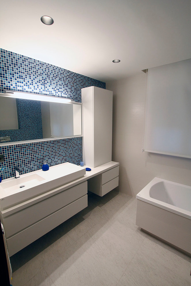 Exemple d'une salle de bain principale tendance de taille moyenne avec un placard à porte plane, des portes de placard blanches, une baignoire en alcôve, WC à poser, un carrelage bleu, des carreaux de céramique, un mur blanc, un sol en carrelage de céramique, une vasque, un plan de toilette en surface solide et un sol beige.
