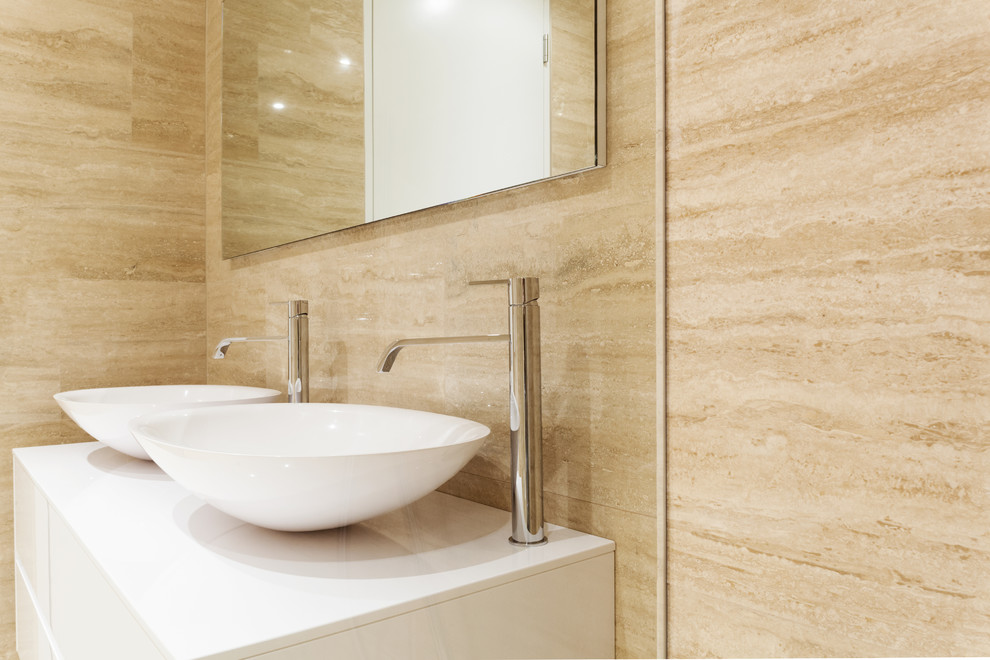Example of a large trendy master beige tile and marble tile marble floor and beige floor bathroom design in Malaga with flat-panel cabinets, white cabinets, a wall-mount toilet, beige walls, a vessel sink, solid surface countertops and white countertops