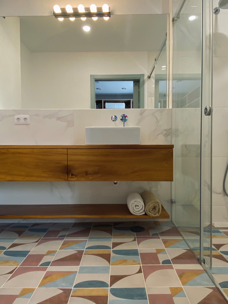 Idéer för att renovera ett mellanstort funkis brun brunt badrum, med släta luckor, skåp i mörkt trä, en kantlös dusch, en vägghängd toalettstol, vit kakel, porslinskakel, vita väggar, mosaikgolv, ett fristående handfat, träbänkskiva, flerfärgat golv och dusch med skjutdörr