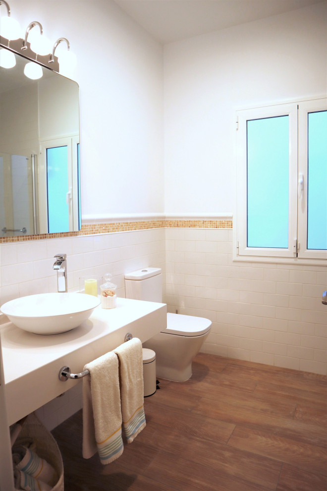 This is an example of a medium sized coastal ensuite bathroom in Other with open cabinets, white cabinets, an alcove shower, a one-piece toilet, white tiles, ceramic tiles, white walls, porcelain flooring, a vessel sink, engineered stone worktops, brown floors, a hinged door and white worktops.