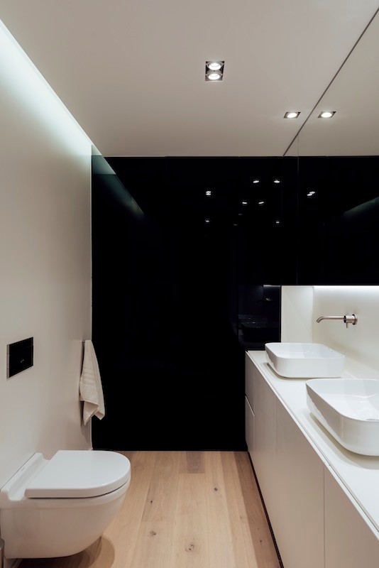 Design ideas for a medium sized modern ensuite bathroom in Other with flat-panel cabinets, an alcove shower, a wall mounted toilet, white walls, light hardwood flooring, a vessel sink, solid surface worktops, a hinged door and white worktops.