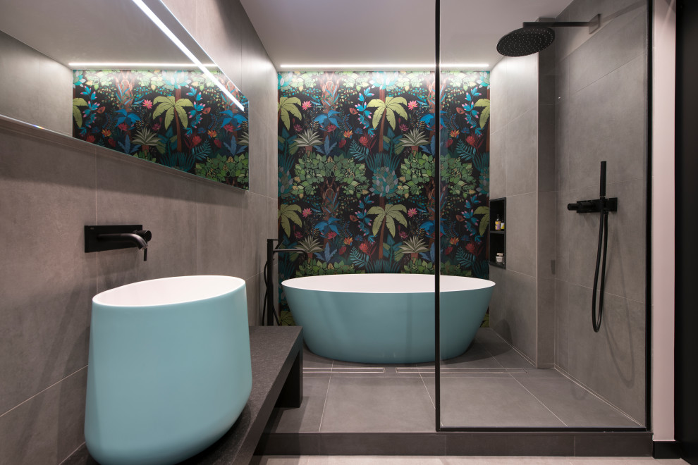 Design ideas for an expansive urban ensuite bathroom in Other with open cabinets, turquoise cabinets, a freestanding bath, a built-in shower, a wall mounted toilet, grey tiles, porcelain tiles, grey walls, porcelain flooring, a vessel sink, grey floors, black worktops, an enclosed toilet, a single sink and a floating vanity unit.