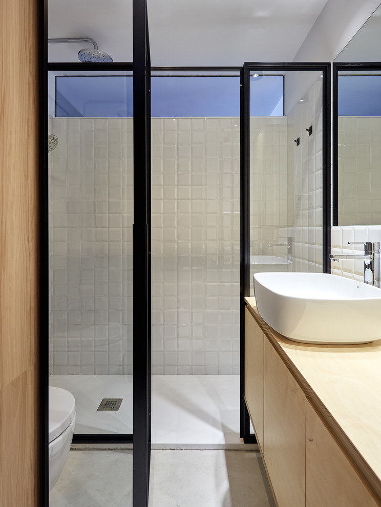 Idéer för ett mellanstort minimalistiskt brun en-suite badrum, med släta luckor, vita skåp, våtrum, en vägghängd toalettstol, vit kakel, tunnelbanekakel, vita väggar, betonggolv, ett fristående handfat, träbänkskiva, grått golv och dusch med gångjärnsdörr