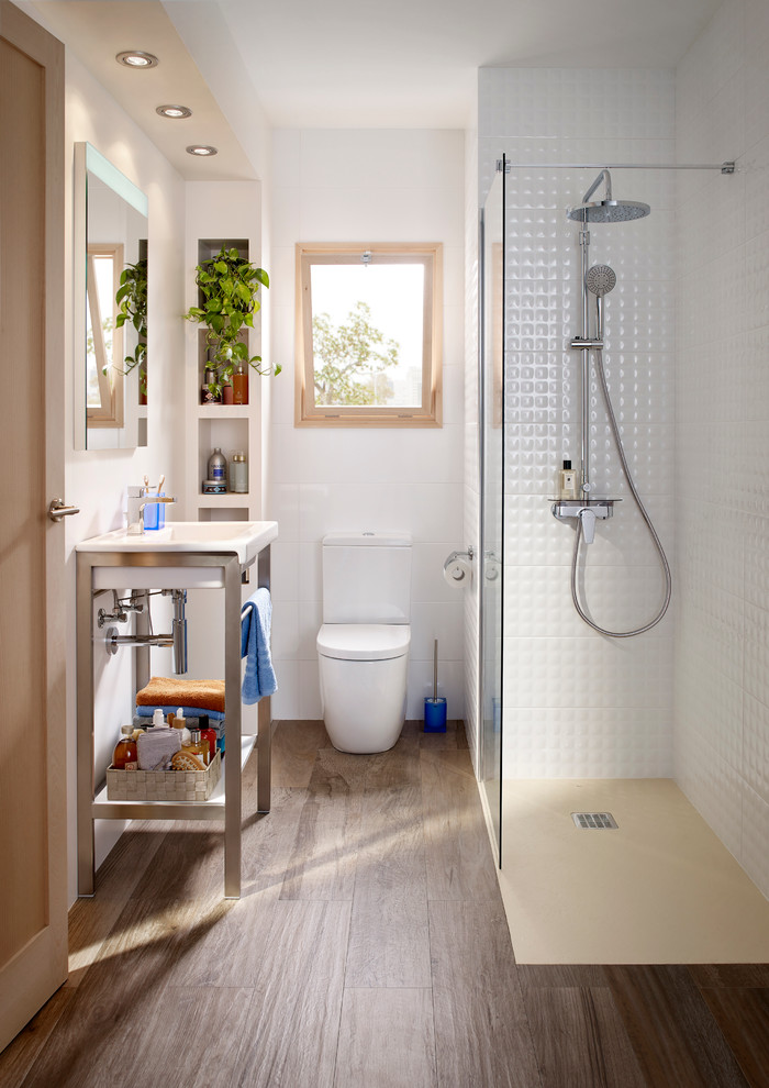 Inredning av ett modernt litet badrum med dusch, med öppna hyllor, en hörndusch, en toalettstol med separat cisternkåpa, vit kakel, vita väggar, mörkt trägolv, ett konsol handfat och med dusch som är öppen