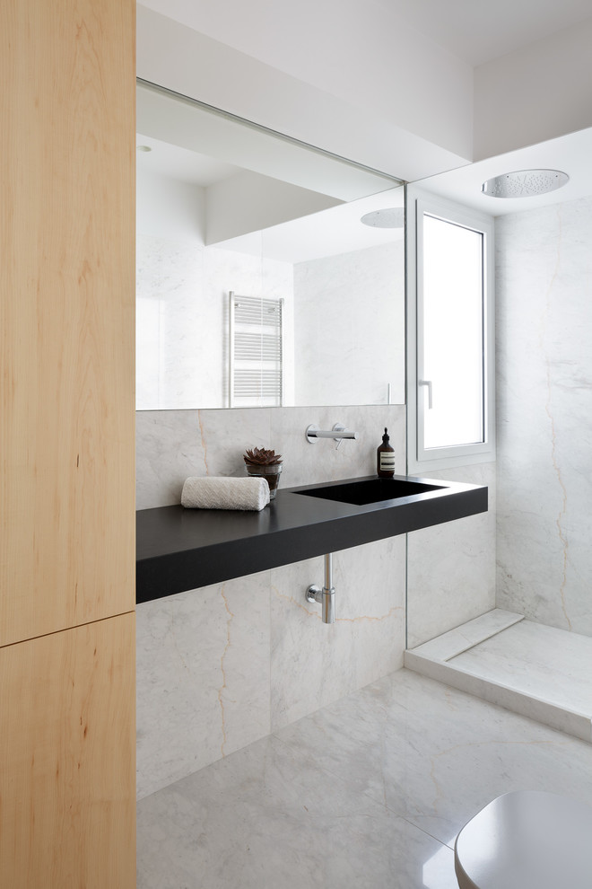 Ispirazione per una stanza da bagno padronale minimalista con doccia aperta, WC sospeso, piastrelle di marmo, pareti bianche, pavimento in marmo, lavabo integrato, pavimento bianco, doccia aperta, top nero e piastrelle bianche