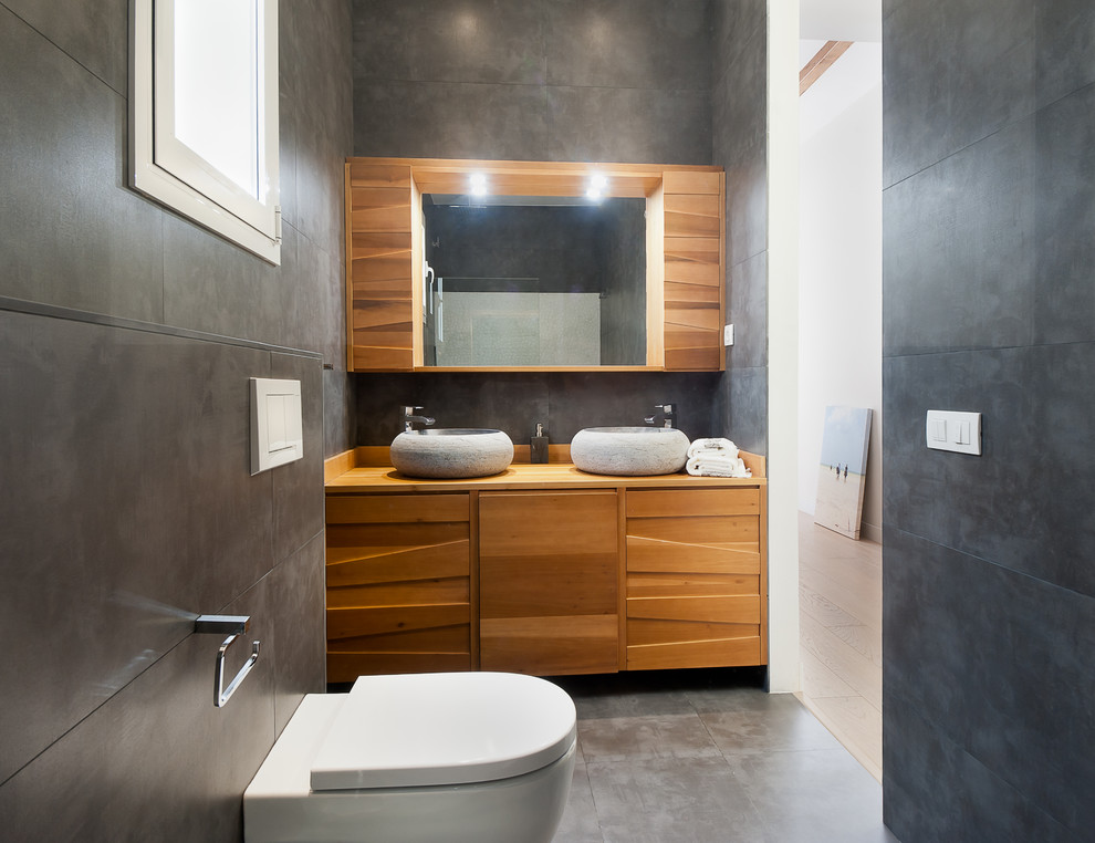 Bild på ett mellanstort funkis en-suite badrum, med luckor med upphöjd panel, skåp i mellenmörkt trä, en vägghängd toalettstol, grå kakel, keramikplattor, grå väggar, klinkergolv i keramik och träbänkskiva