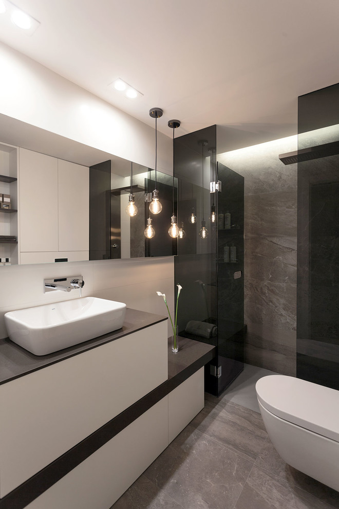 Small modern ensuite bathroom in Valencia with recessed-panel cabinets, white cabinets, a built-in shower, a wall mounted toilet, grey tiles, ceramic tiles, white walls, ceramic flooring, a vessel sink, engineered stone worktops, grey floors and a hinged door.