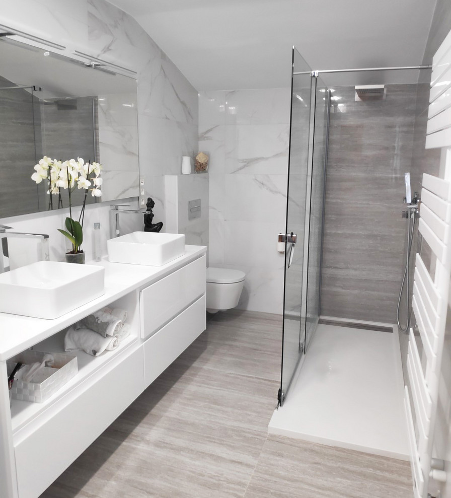 This is an example of a medium sized traditional ensuite bathroom in Bilbao with freestanding cabinets, white cabinets, a walk-in shower, a wall mounted toilet, black and white tiles, ceramic tiles, multi-coloured walls, travertine flooring, solid surface worktops, beige floors, a hinged door and white worktops.