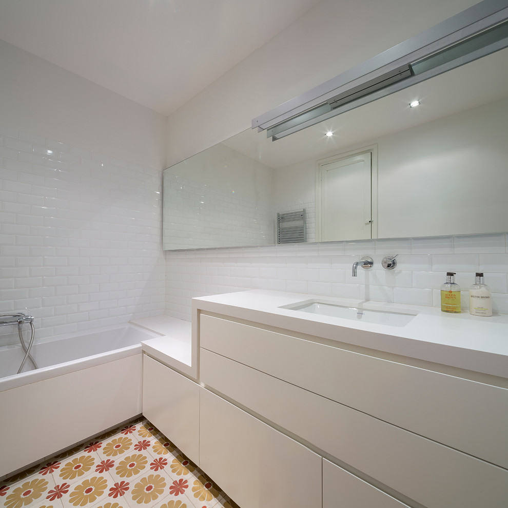 Inredning av ett minimalistiskt mellanstort en-suite badrum, med släta luckor, vita skåp, ett badkar i en alkov, en dusch/badkar-kombination, vit kakel, tunnelbanekakel, vita väggar, klinkergolv i keramik och ett undermonterad handfat