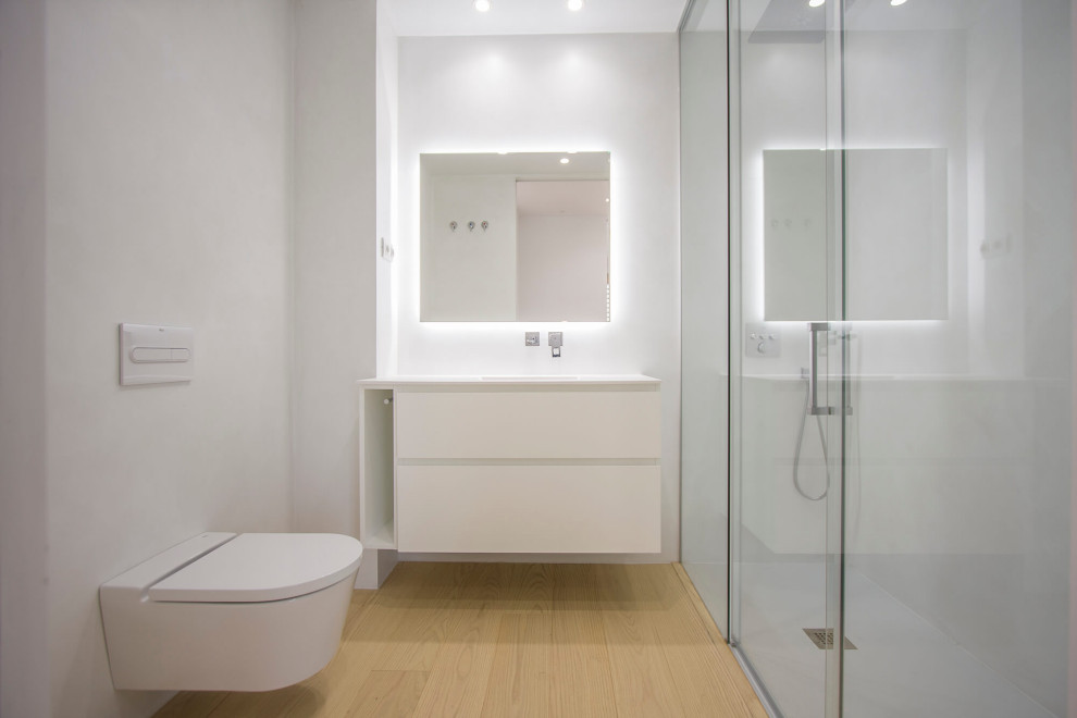 Idee per una piccola stanza da bagno padronale moderna con ante lisce, ante bianche, WC monopezzo, piastrelle bianche, piastrelle di cemento, pareti bianche, parquet chiaro, toilette e un lavabo