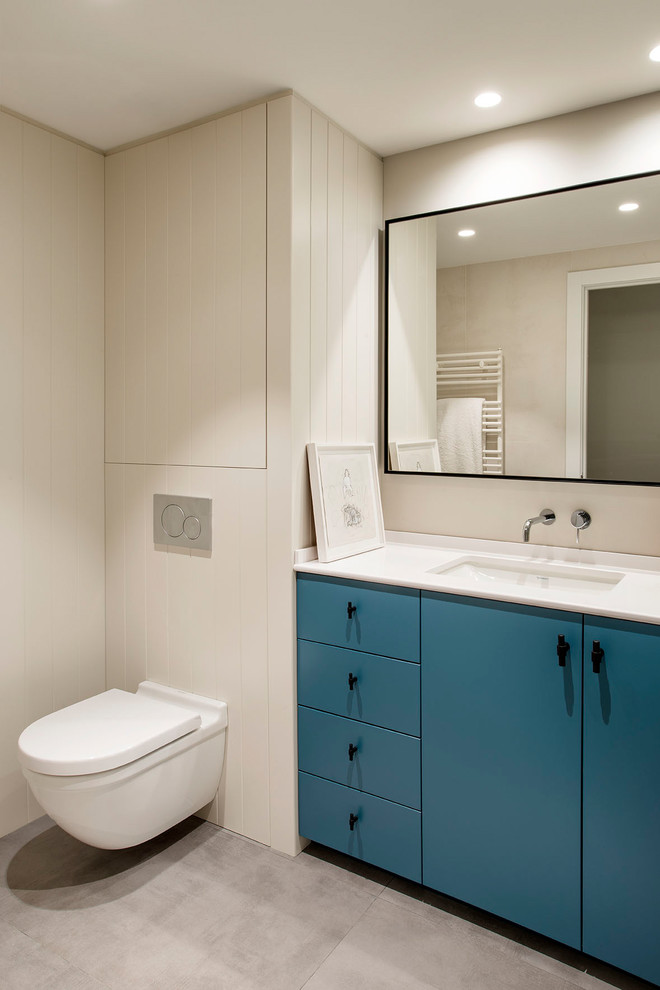 Skandinavisches Badezimmer mit blauen Schränken, Wandtoilette, grauem Boden, weißer Waschtischplatte, beiger Wandfarbe, Unterbauwaschbecken und flächenbündigen Schrankfronten in Barcelona
