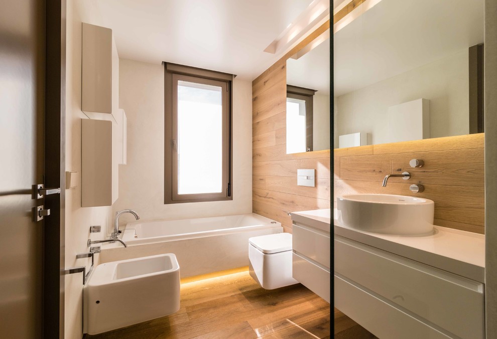 Modern inredning av ett mellanstort en-suite badrum, med ett fristående handfat, släta luckor, vita skåp, en bidé, mellanmörkt trägolv, bänkskiva i akrylsten, flerfärgade väggar och ett platsbyggt badkar