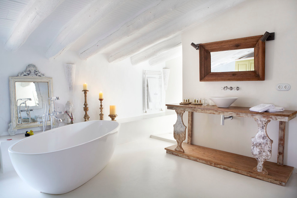 Cette image montre une grande salle de bain principale méditerranéenne en bois brun avec un placard sans porte, une baignoire indépendante, un combiné douche/baignoire, un mur blanc, sol en béton ciré, une vasque et un plan de toilette en bois.