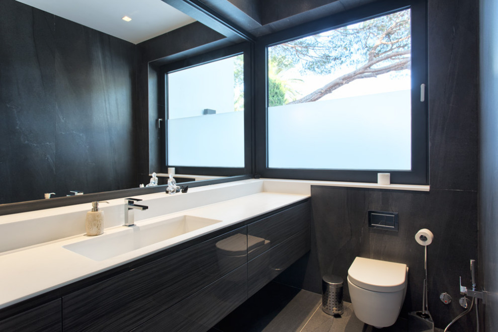 Inspiration pour une salle de bain longue et étroite design avec un placard à porte plane, des portes de placard noires, WC suspendus, un carrelage noir, un lavabo intégré, un sol gris et un plan de toilette blanc.