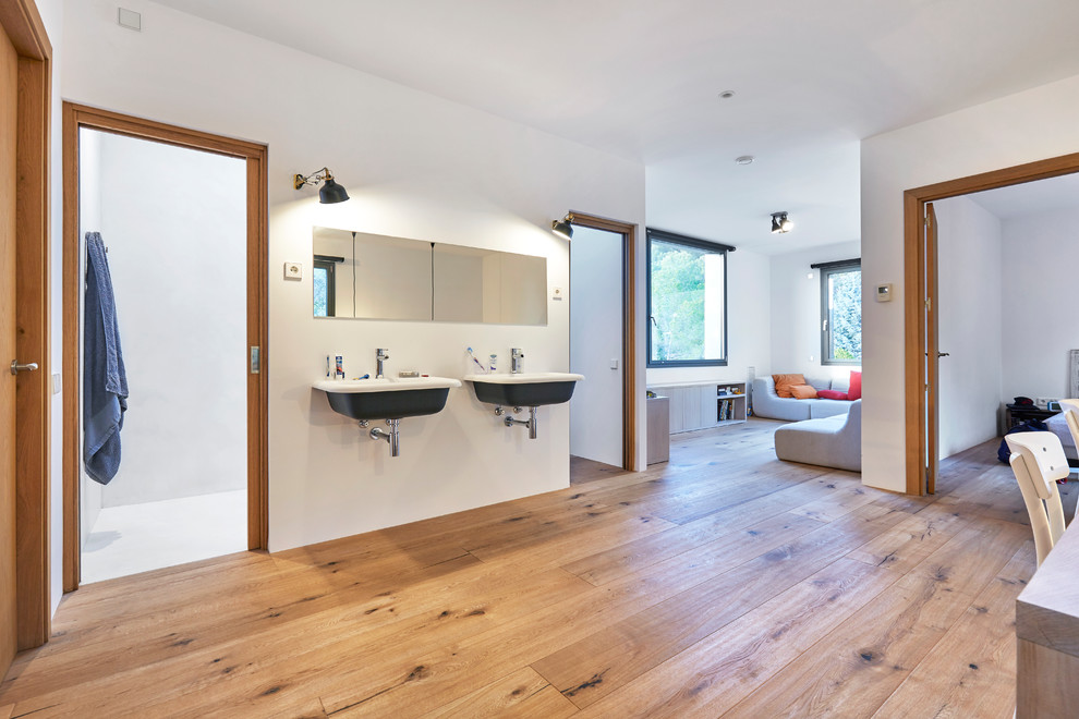 Cette image montre une salle de bain design avec un mur blanc, un sol en bois brun, un lavabo suspendu et un sol marron.