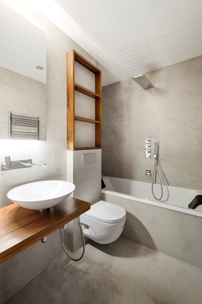 На фото: ванная комната в современном стиле с ванной в нише, душем над ванной, инсталляцией, серыми стенами, бетонным полом, настольной раковиной, столешницей из дерева, серым полом, коричневой столешницей и открытым душем с
