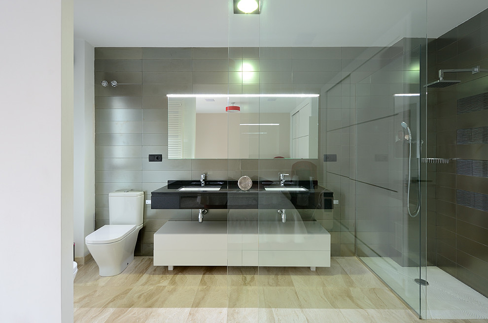 Стильный дизайн: большая ванная комната в современном стиле с плоскими фасадами, белыми фасадами, угловым душем, раздельным унитазом, серой плиткой, керамической плиткой, серыми стенами, полом из травертина, душевой кабиной, врезной раковиной и столешницей из искусственного камня - последний тренд