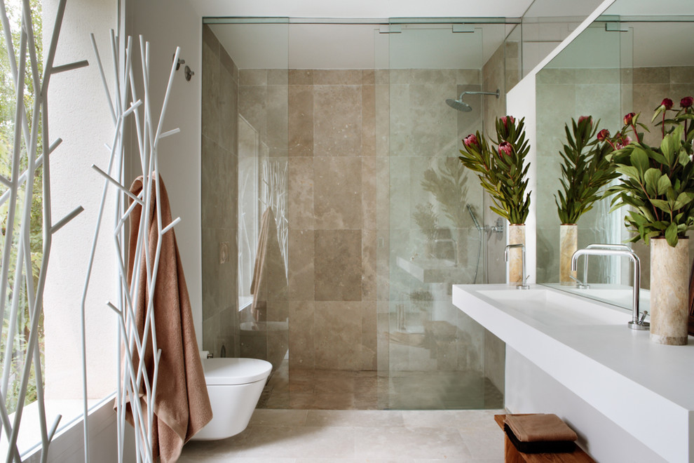 Inspiration för ett mellanstort funkis badrum med dusch, med en dusch i en alkov, en vägghängd toalettstol, stenkakel, vita väggar, travertin golv, ett avlångt handfat och bänkskiva i akrylsten