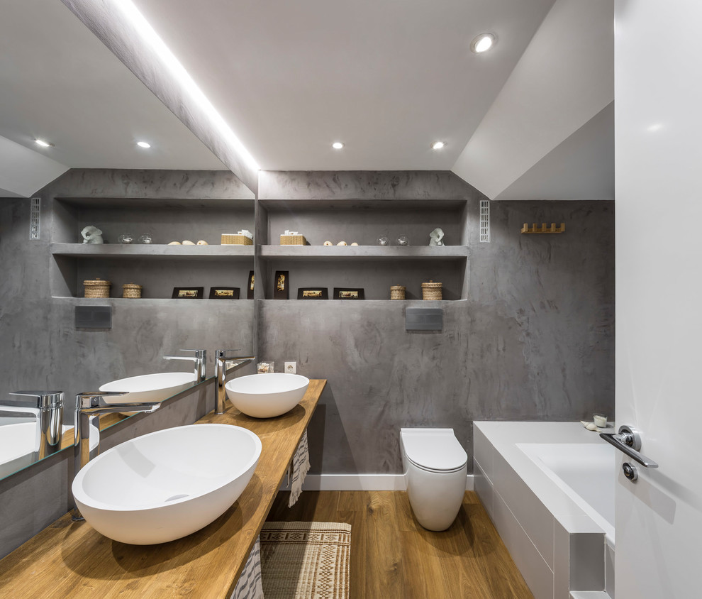 Foto de cuarto de baño actual con bañera encastrada, paredes grises, lavabo sobreencimera y encimera de madera