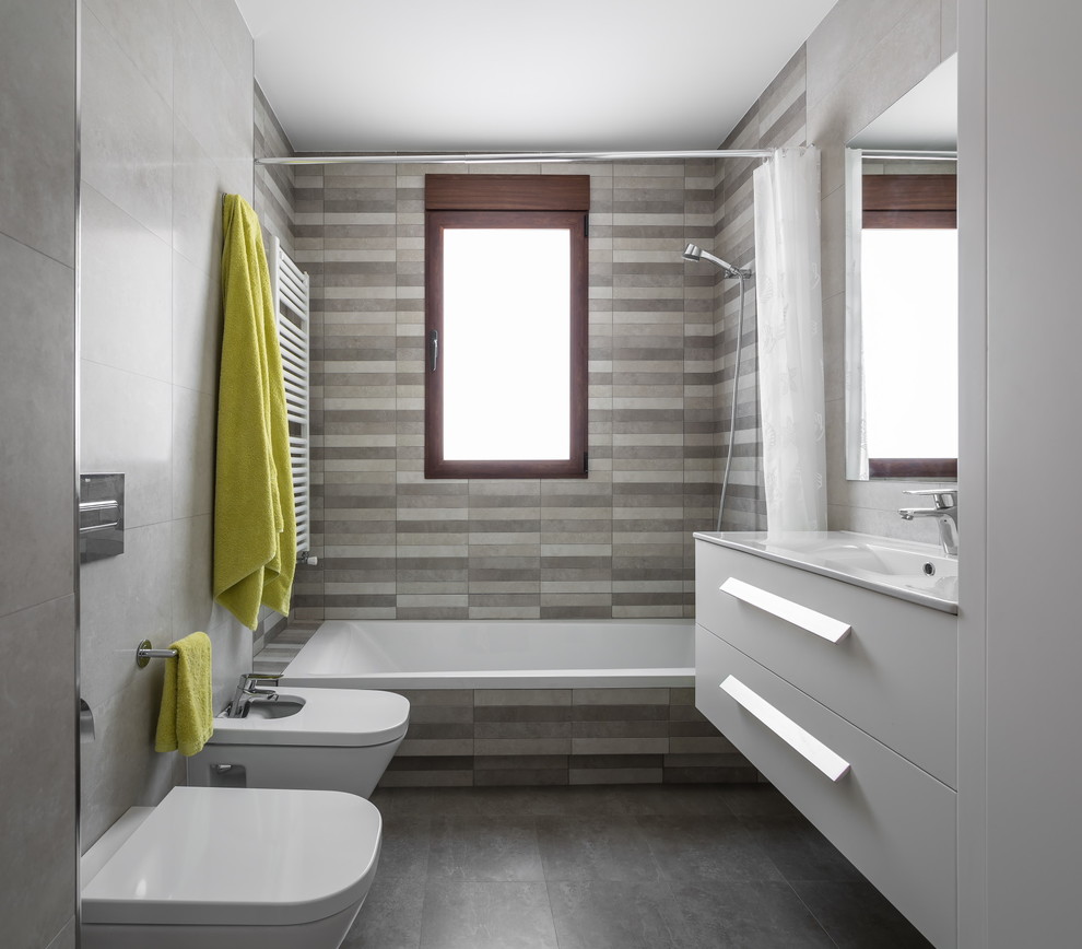 This is an example of a small contemporary grey and white bathroom in Valencia with flat-panel cabinets, white cabinets, a shower/bath combination, a wall mounted toilet, mosaic tiles, multi-coloured walls, slate flooring, an integrated sink, solid surface worktops, grey tiles and a built-in bath.