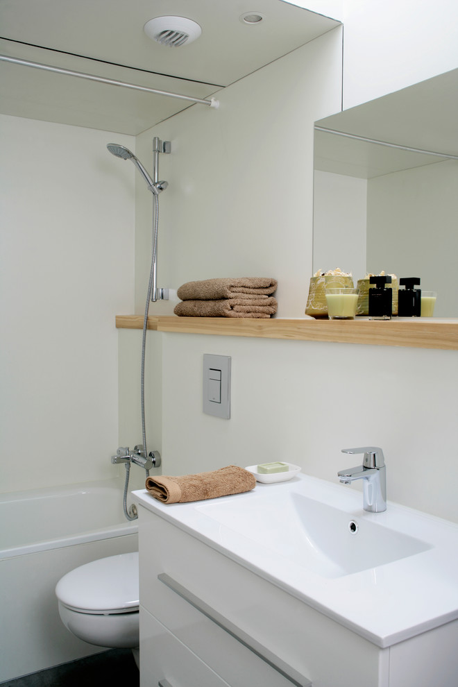 Modelo de cuarto de baño escandinavo de tamaño medio con armarios con paneles lisos, puertas de armario blancas, bañera empotrada, combinación de ducha y bañera, sanitario de dos piezas, paredes blancas, aseo y ducha y lavabo integrado