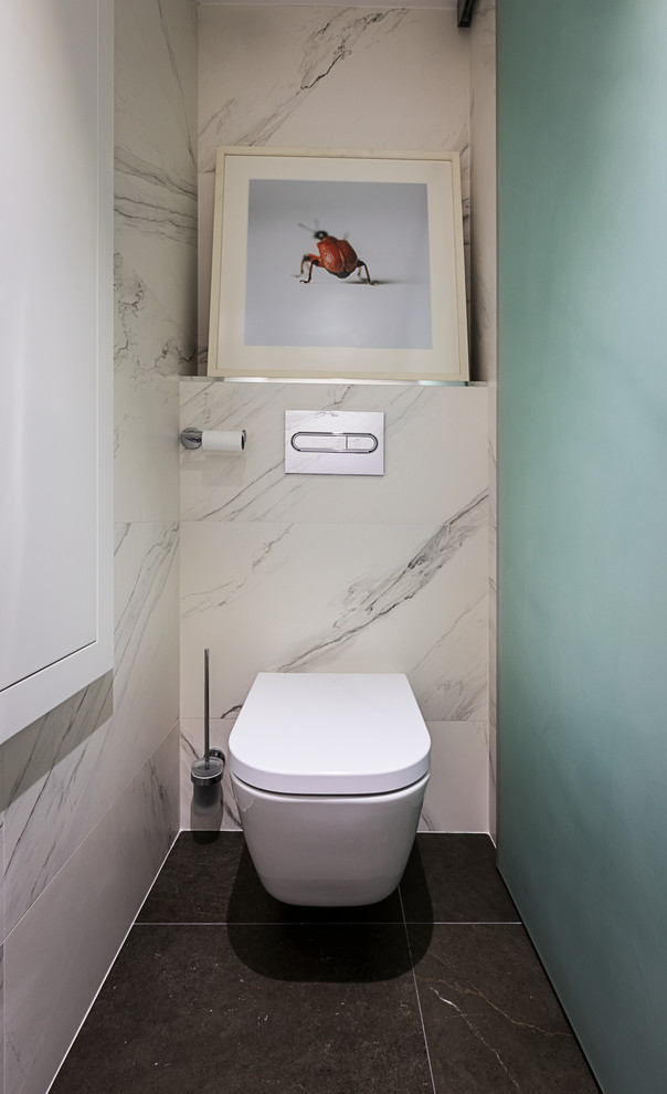 This is an example of a medium sized contemporary cloakroom in Madrid with freestanding cabinets, grey cabinets, a wall mounted toilet, white tiles, porcelain tiles, grey walls, porcelain flooring, a built-in sink, solid surface worktops and grey floors.