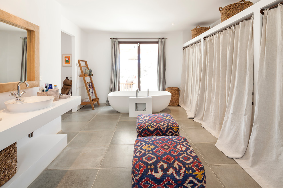 На фото: огромная главная ванная комната в средиземноморском стиле с открытыми фасадами, белыми фасадами, отдельно стоящей ванной, душем над ванной, белыми стенами, полом из керамической плитки, настольной раковиной и серым полом