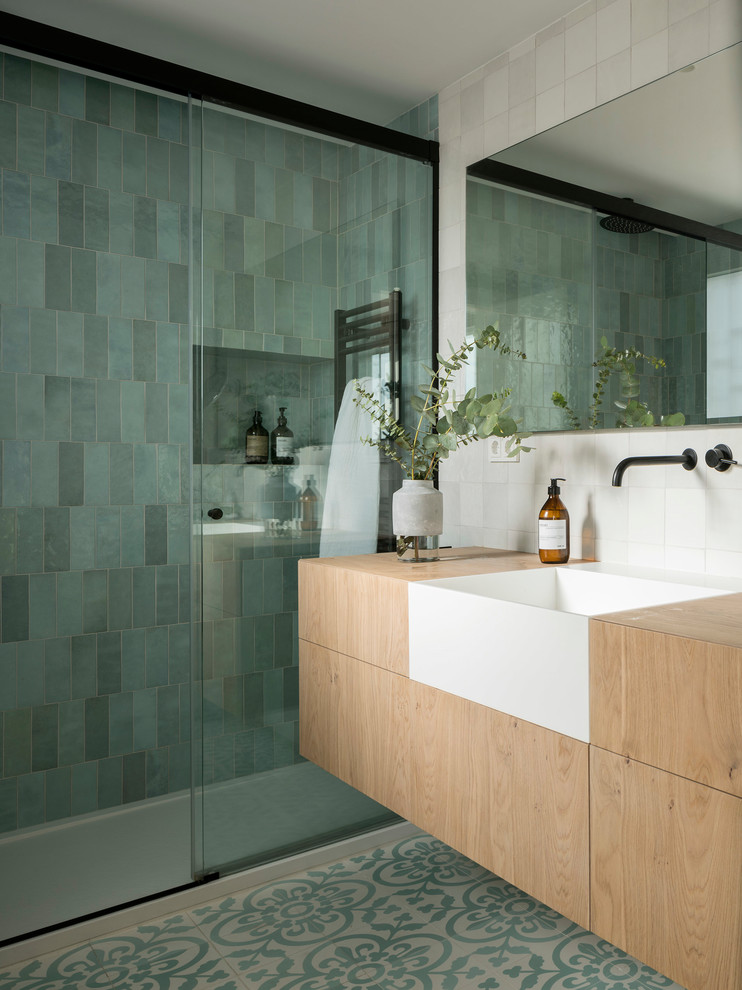 Cette image montre une salle de bain nordique en bois clair de taille moyenne avec un placard à porte plane, un carrelage vert, un plan de toilette en bois, un sol multicolore et une cabine de douche à porte coulissante.